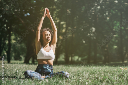 sporty young woman meditates sitting on the grass.