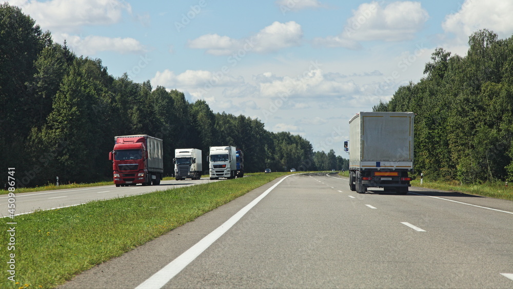 Two European semi trucks on suburban highway with grassy safety lane at Sunny summer day on blue cloudy sky background, beautiful road landscape