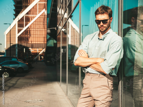 Portrait of handsome confident stylish hipster lambersexual model.Modern man dressed in shirt. Fashion male posing in the street background near skyscrapers in sunglasses