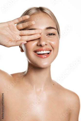 Natural beauty. Feminine blond girl laughing with white, perfect smile, looking happy, touching hydrated, glowing facial skin, head and shoulders portrait, studio background