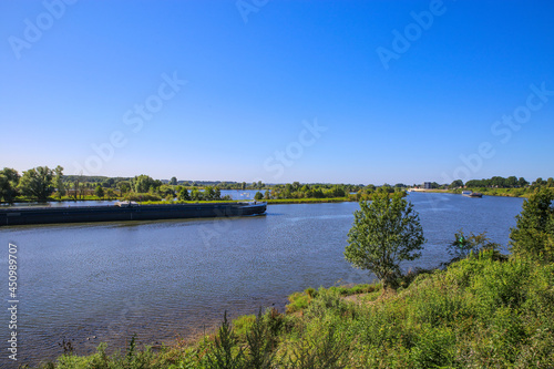 View over green rural landscape on river Maas with inland waterway vessel against blue summer sky - Between Roermond and Venlo, Netherlands photo