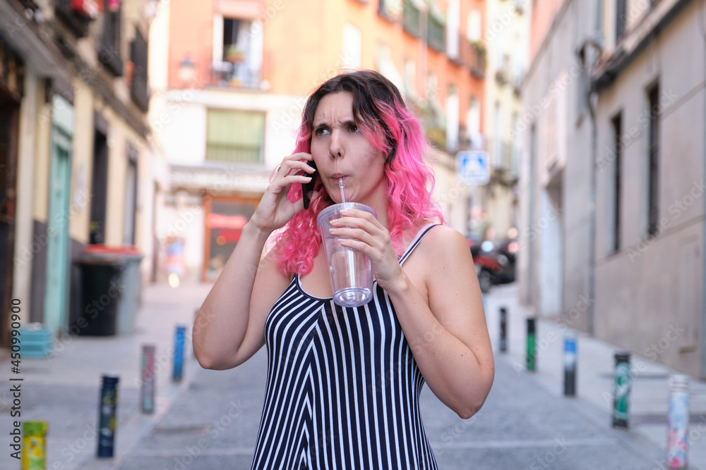 Young caucasian woman with pink hair frowning while talking on the phone.