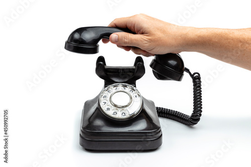 Foto MALE HAND LIFTING OLD ROTARY DIAL BLACK PHONE ISOLATED ON WHITE BACKGROUND