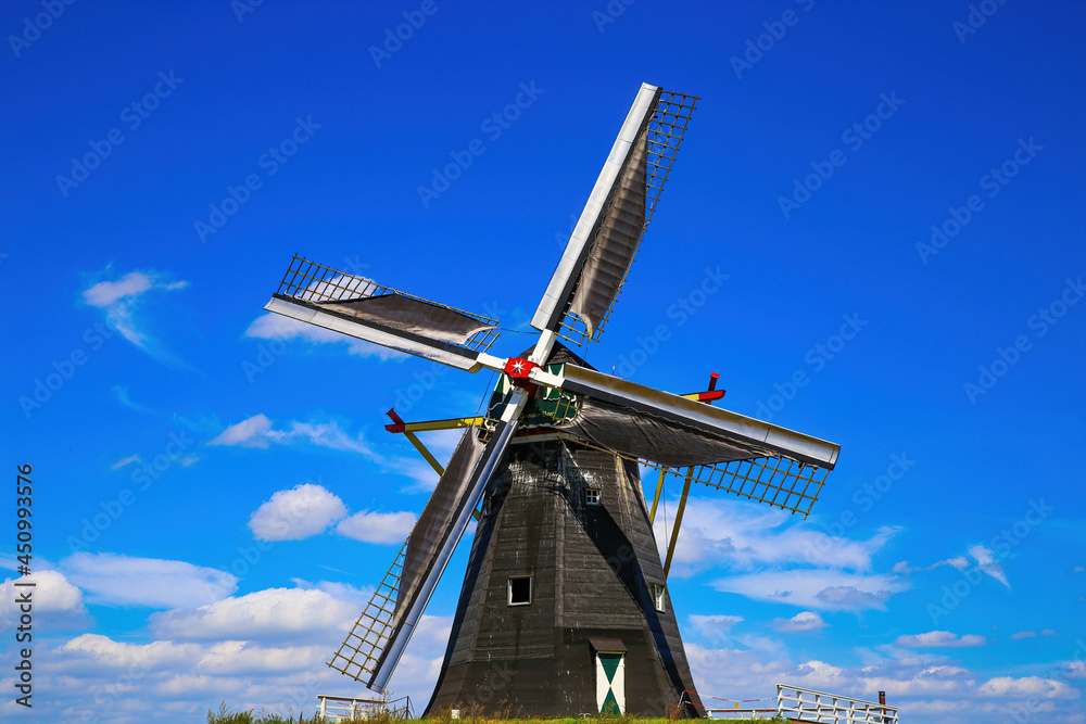 Beesel, Netherlands - July 9. 2021: View on isolated typical dutch windmill (Molen de grauwe beer) in rural landscape against deep blue summer sky with cumulus clouds
