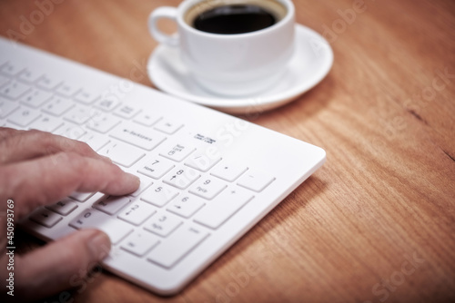 Woman works in the office on a wooden table. Woman's hand on keyboard. Concept workspace, working at a computer, freelance, design. Cayboard and cup of coffee. Flat lay, top view.