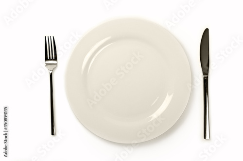 Empty white plate with fork and knife on table. Top view.