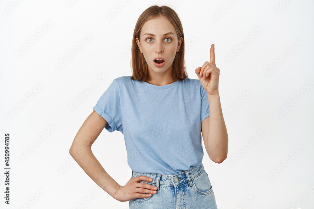 Image of excited blond woman pitching an idea, raising finger and gasp eureka, has great plan, tell her suggestion, standing in blue t-shirt against white background Image of excited blond woman pitching an idea, raising finger and gasp eureka, has great plan, tell her suggestion, standing in blue t-shirt against white background