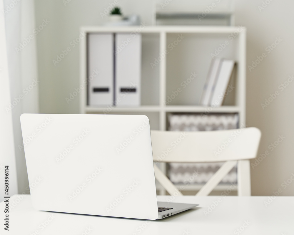 Contemporary minimalist interior. Mockup of office at home. White laptop, chair and bookshelf. Freelance desk. Distance education. Online learning, teleworking, online lectures. Concept of home office Contemporary minimalist interior. Mockup of office at home. White laptop, chair and bookshelf. Freelance desk. Distance education. Online learning, teleworking, online lectures. Concept of home office