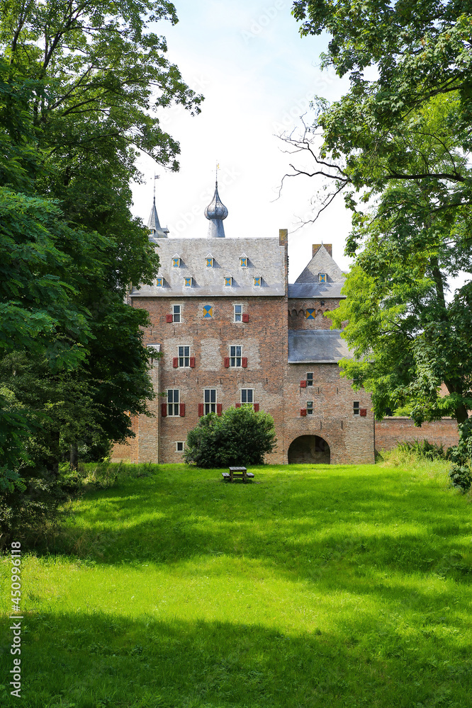 View beyond green trees on dutch water castle from 14th century against blue summer sky