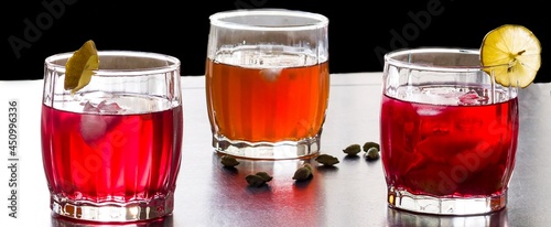 Front view of glasses of Sangria fruit punch,a blend of Kokam juice and Kahwa green tea garnished with lime slice. Close up view of back lit summer drink on wood surface and against black background .
