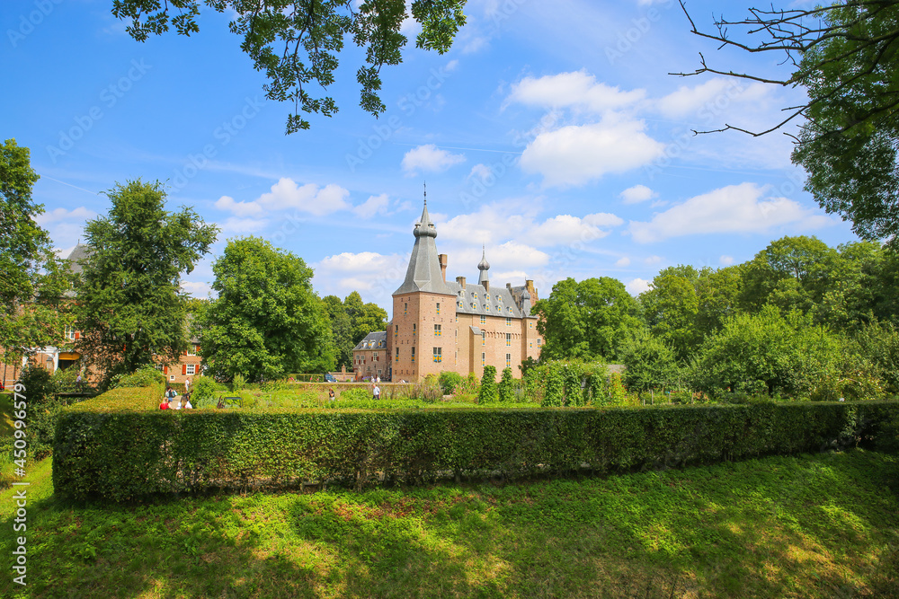 View over garden hedge on medieval dutch castle from 14th century with green trees agaisnt blue summer sky