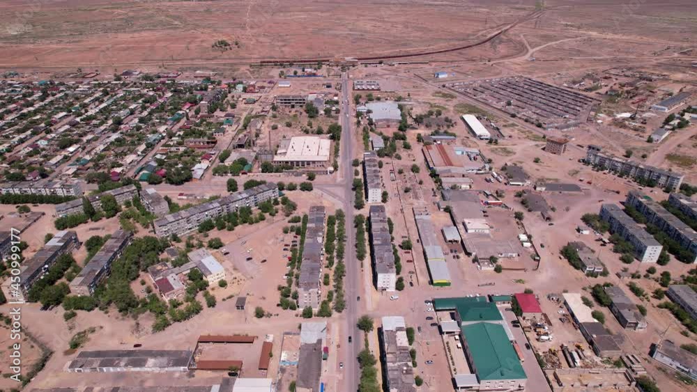 Drone view of the small town of Balkhash. The city is located on the shore of a lake. Low houses, free streets and roads. Green trees grow and there are sports grounds. There is a steppe around city Drone view of the small town of Balkhash. The city is located on the shore of a lake. Low houses, free streets and roads. Green trees grow and there are sports grounds. There is a steppe around city