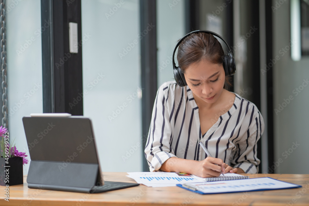 Businesswoman writing a note while using laptop at a table in an office. Businesswoman writing a note while using laptop at a table in an office.
