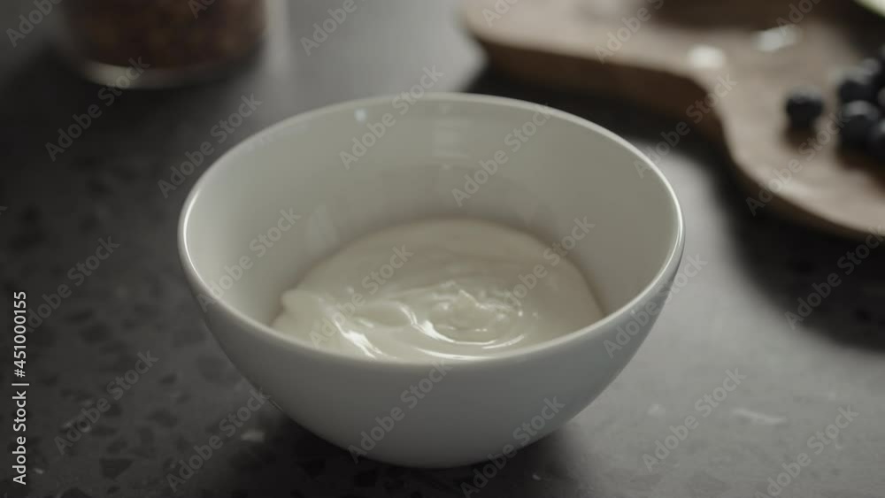 Pour yogurt in white bowl on concrete countertop Pour yogurt in white bowl on concrete countertop