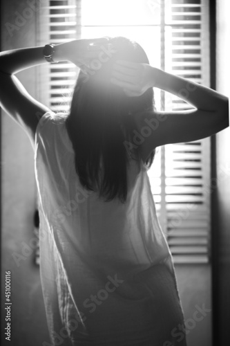 Monochrome back portrait of sexy girl puts her hands on the head with sunlight and blurred curtain in background