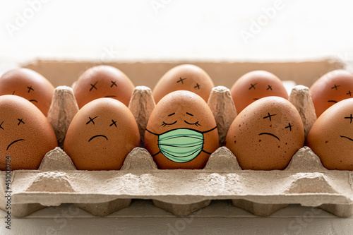 Egg with a content face wearing a protective face mask, sitting in a row next to eggs that are dead. A conceptual image relating to Covid 19, the best way to avoid catching the virus.	