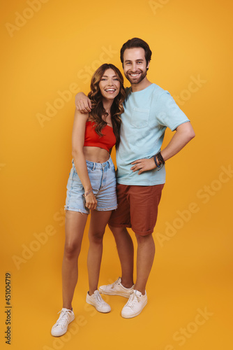 Full length of beautiful young couple embracing while standing against yellow background © gstockstudio