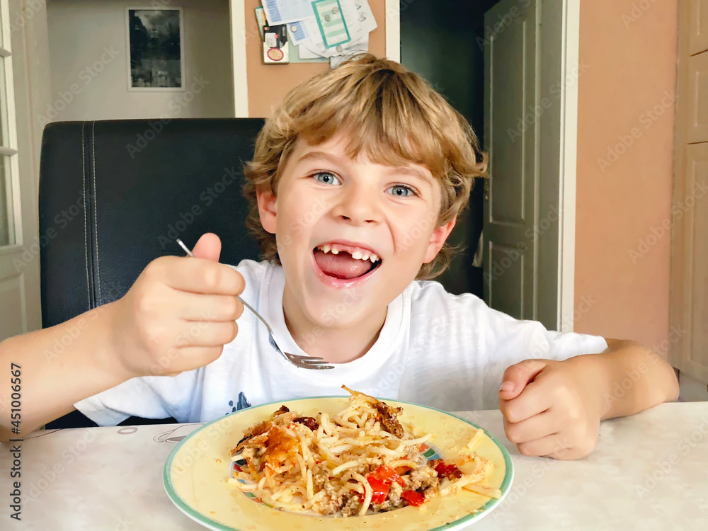 Little happy school boy eating pasta noodles and spaghetti. Cute child with tooth gap in domestic home kitchen, having lunch after school. Little happy school boy eating pasta noodles and spaghetti. Cute child with tooth gap in domestic home kitchen, having lunch after school.