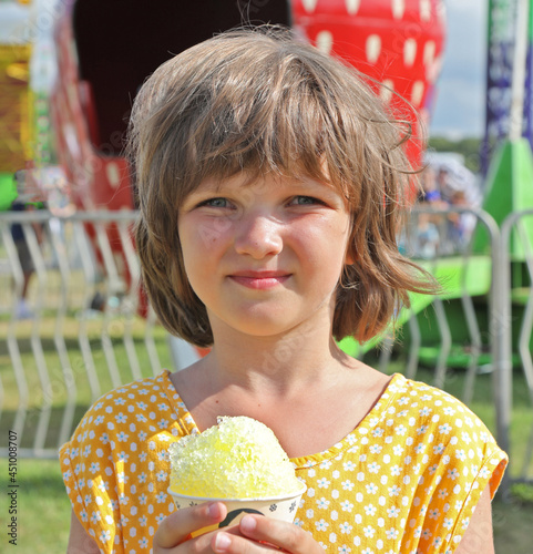 Girl in a yellow dress looks at the camera and holds a cone with Italian ice in her hands. photo