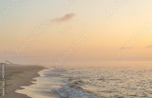 Fototapeta Naklejka Na Ścianę i Meble -  Foggy sunrise over the sea. Pastel shades. Beautiful landscape. Sandy beach of the ocean. Sunset sky. Clouds. Coast.