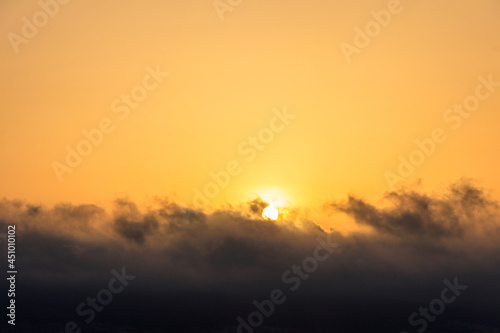 Beautiful rising orange sun above the clouds in sky at sunrise © olyasolodenko