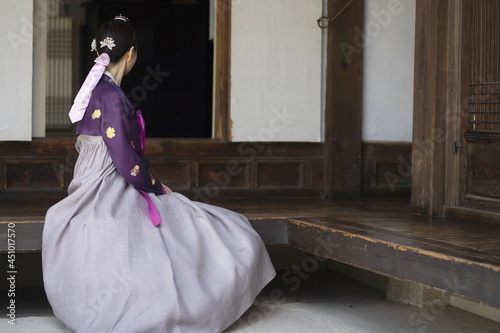 Woman in Korean traditional clothes sitting on traditional house
