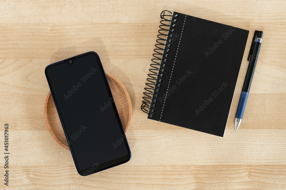 Smart phone, notebook and pen in black color, on wood background. Office style. Smart phone, notebook and pen in black color, on wood background. Office style.