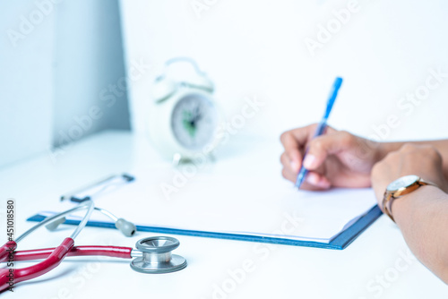 The doctor is writing the patient's condition diary. on the white table There is a stethoscope and recording paper in the office at the hospital.