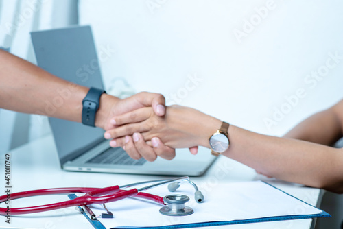 The doctor holds the patient's arm and diagnoses the disease on a white table. There is a stethoscope and recording paper in the office at the hospital.