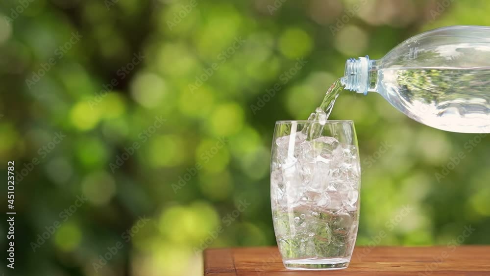 water from plastic bottle pouring into glass with ice cubes