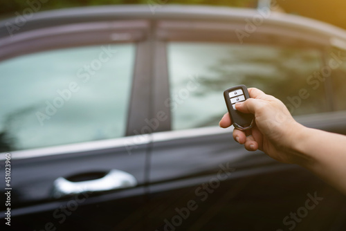 Female hand holding and pushing car remote control to lock or unlock the car.