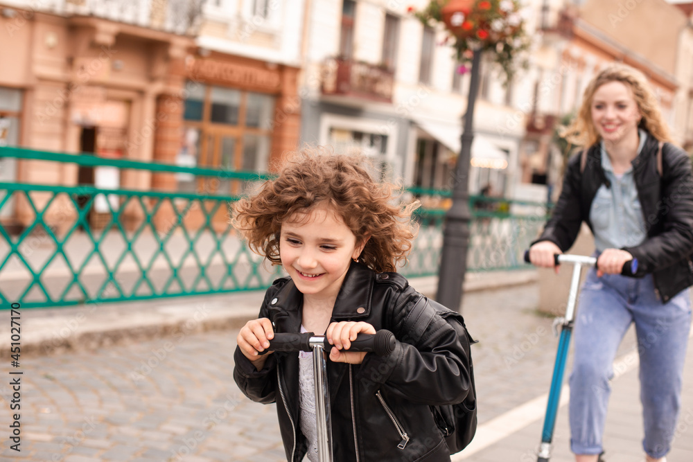 Fototapeta premium The girl rides a scooter for the first time together with her mom