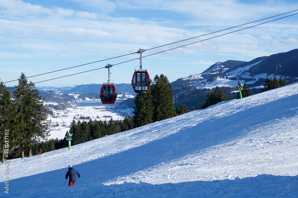 OBERSTAUFEN, GERMANY - 31 DEC, 2017: Ski lift with gondola and ski slope and skiers in the foreground OBERSTAUFEN, GERMANY - 31 DEC, 2017: Ski lift with gondola and ski slope and skiers in the foreground