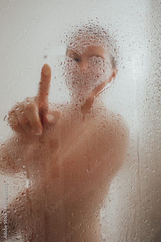 Fototapeta premium Cheerful woman drawing heart on condensed glass door