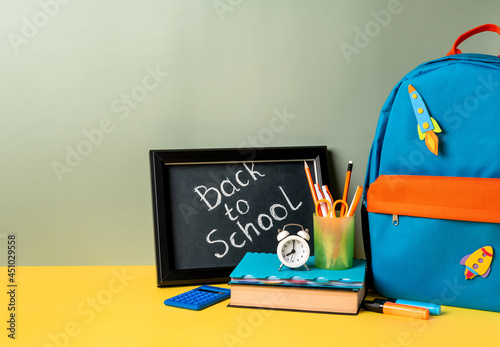 School backpack with colorful school supplies and blackboard with letters back to school. School supplies on green background. Banner design. Back to school, education concept.