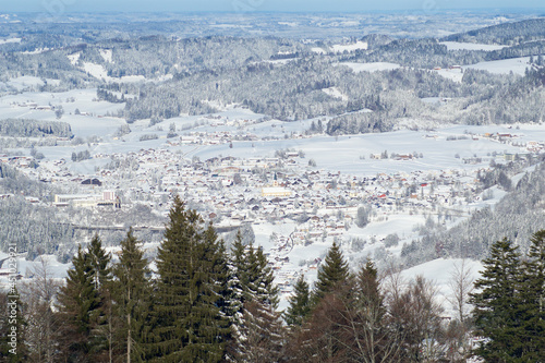 OBERSTAUFEN, GERMANY - 29 DEC, 2017: Wonderful view of the snow-covered winter sports resort of Oberstaufen in the Bavarian Alps with green coniferous trees in the foreground