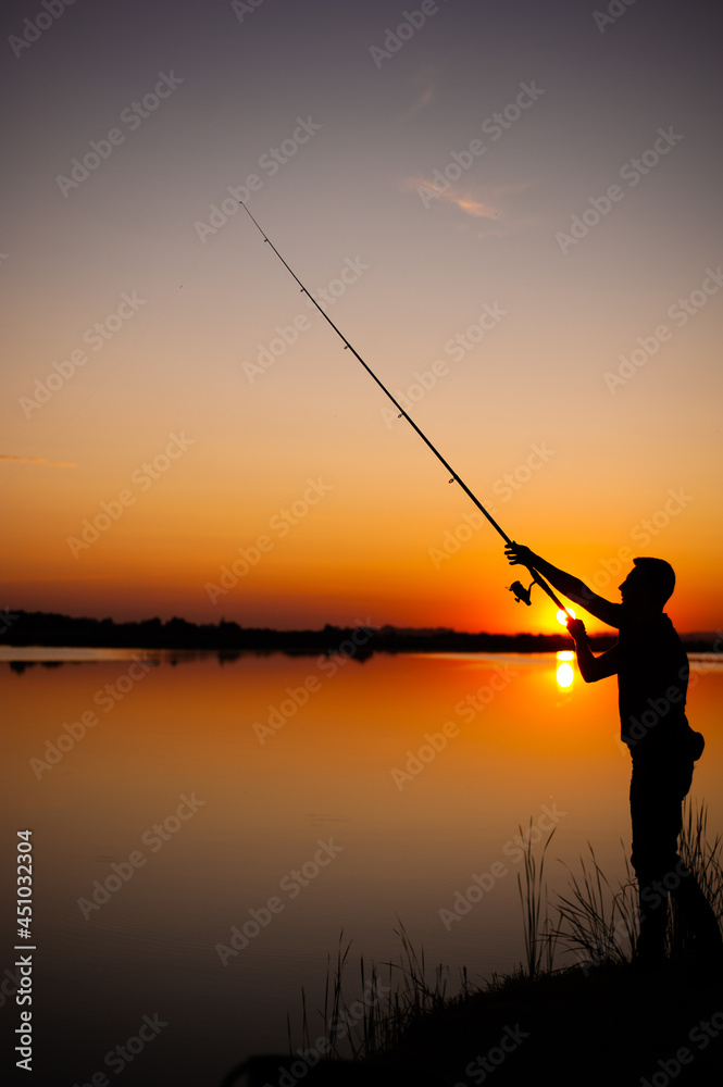 A fisherman silhouette fishing at sunset. Freshwater fishing, catch of fish