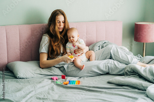 Beautiful red-haired mom in pajamas with a newborn baby on the bed in the bedroom plays