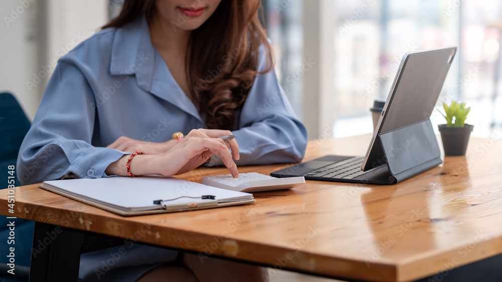 Close-up woman hand using a calculator with document and tablet placed at the office.