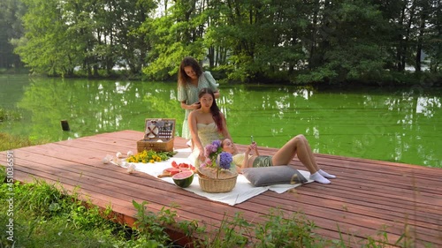 Arc shot three female is having  picnic time. Caucasian young woman is braiding a pigtail of an asian girl on summer day outdoor
