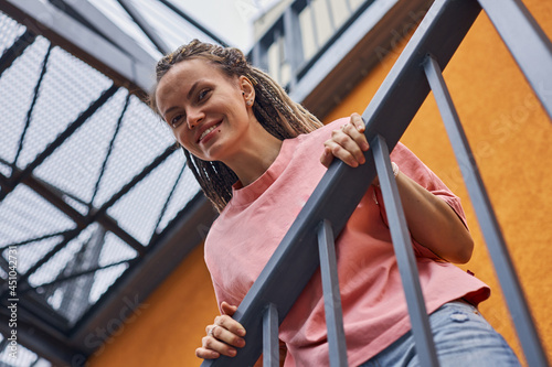 cheerful girl with pigtails stands leaning on an iron staircase against the background of a bright orange wall. High quality photo