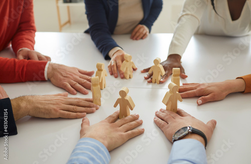 Group of multiracial business people working together arrange human figures in circle on table. Team of multiethnic workmates join little wooden figures as teamwork, community and collaboration symbol
