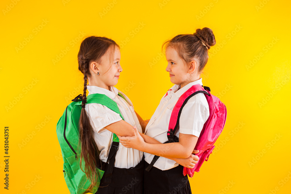 Two smiling schoolgirls in uniform are hugging at the yellow Two smiling schoolgirls in uniform are hugging at the yellow