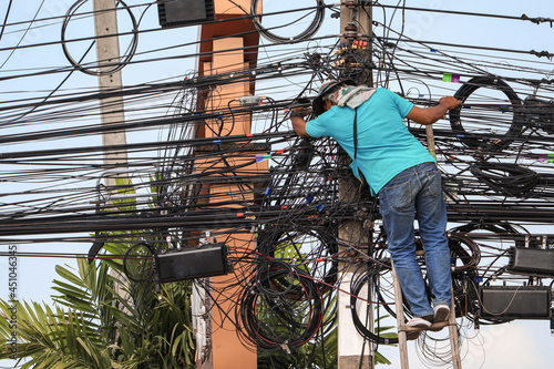 An electrician is climbing an electric pole to inspect and install wires without wearing protective equipment for safety from work risks.