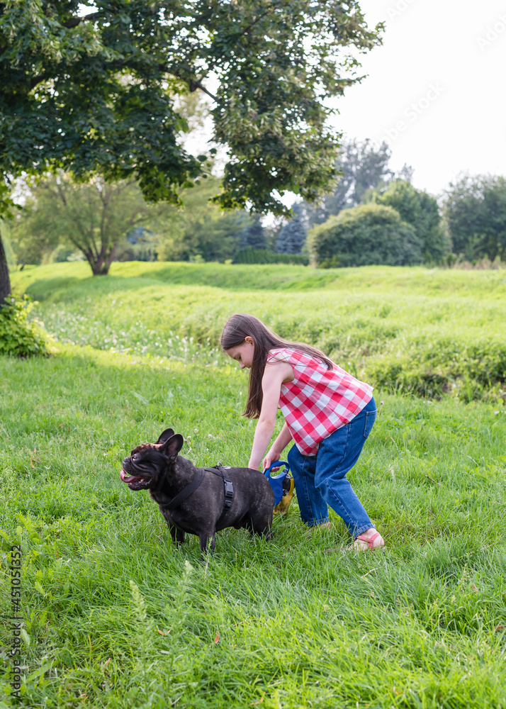 Girl 6 years old on a walk with the dog. Girl and French Bulldog. A little girl stroking a dog in the park.