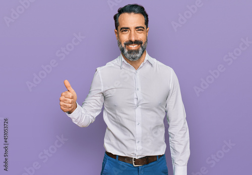 Middle aged man with beard wearing casual white shirt smiling happy and positive, thumb up doing excellent and approval sign