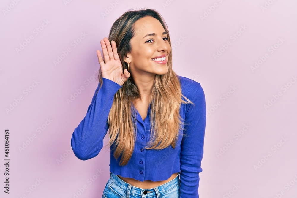 Beautiful hispanic woman wearing casual blue shirt smiling with hand over ear listening an hearing to rumor or gossip. deafness concept. Beautiful hispanic woman wearing casual blue shirt smiling with hand over ear listening an hearing to rumor or gossip. deafness concept.