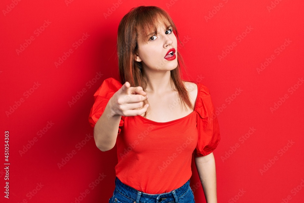 Redhead young woman wearing casual red t shirt pointing displeased and frustrated to the camera, angry and furious with you Redhead young woman wearing casual red t shirt pointing displeased and frustrated to the camera, angry and furious with you