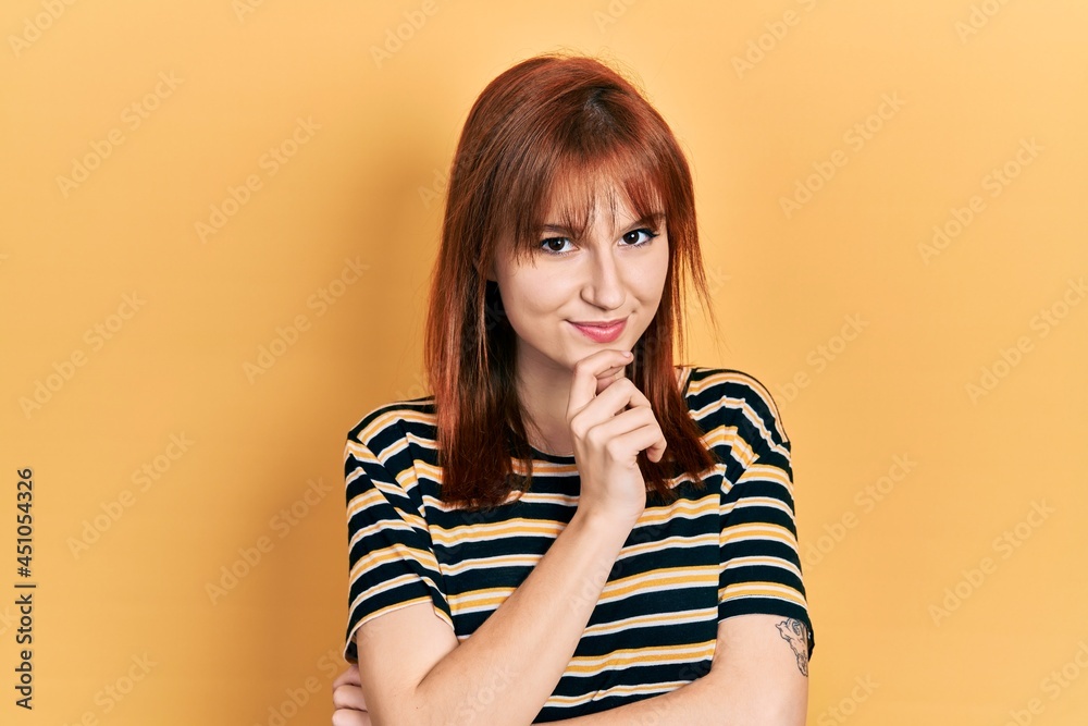 Redhead young woman wearing casual striped t shirt smiling looking confident at the camera with crossed arms and hand on chin. thinking positive. Redhead young woman wearing casual striped t shirt smiling looking confident at the camera with crossed arms and hand on chin. thinking positive.