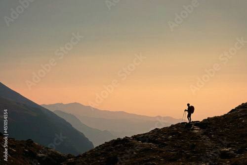 Small silhouette of tourist with backpack on the rocky mountain slope. Beauty of nature, tourism and travel concept